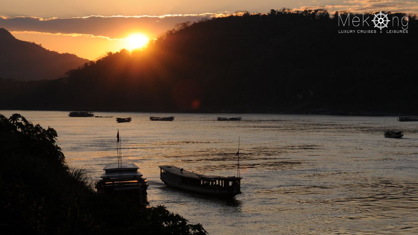 Sunset over the Mekong River with traditional boats in Laos