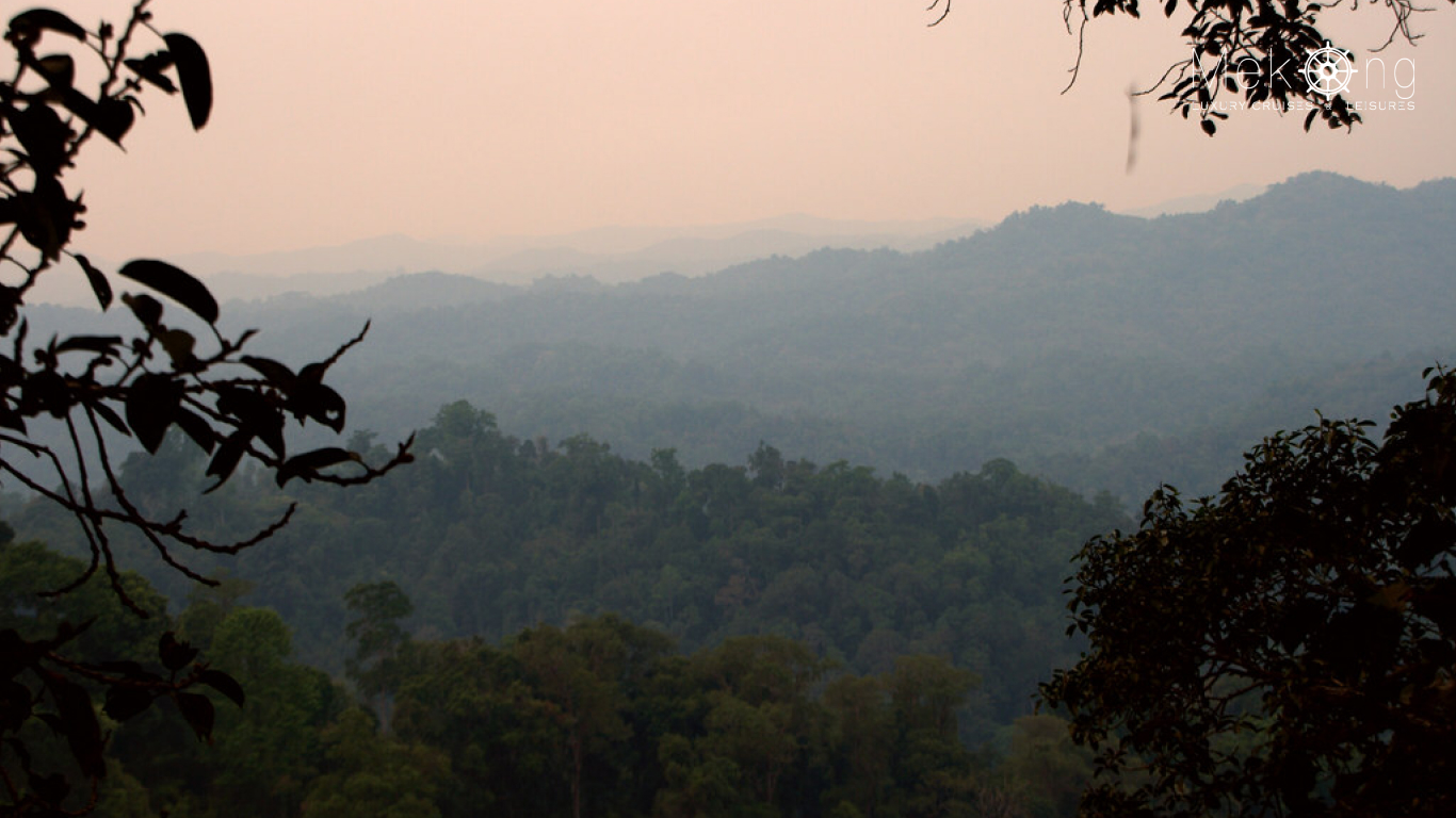 Smoky haze softening forested hills under a pinkish sky in northern Laos during the March burning season