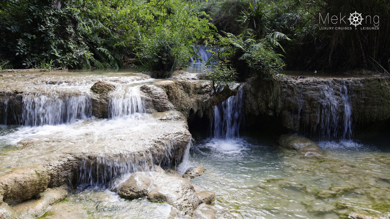Small cascades spilling into clear turquoise pools surrounded by green forest at Kuang Si Falls near Luang Prabang
