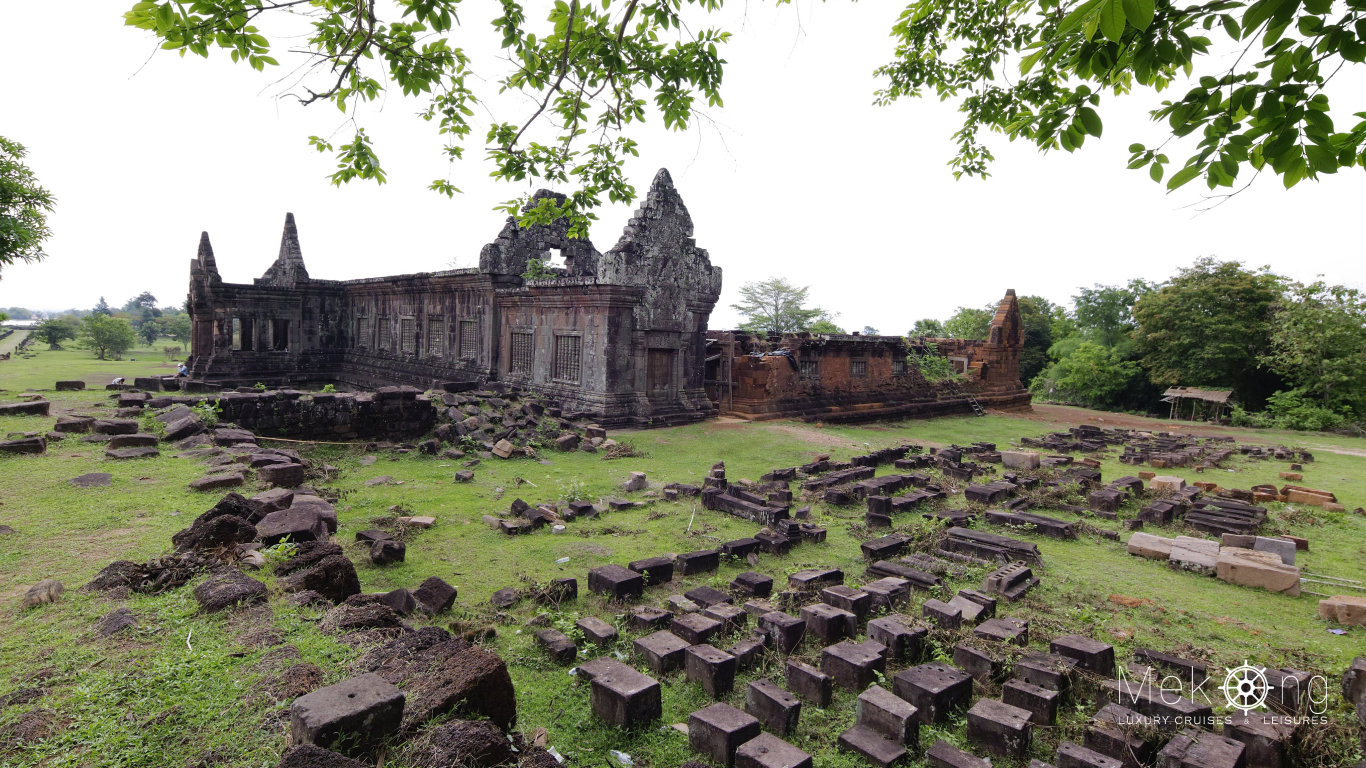 Ancient Khmer sanctuary ruins at Wat Phou, with scattered stone blocks on a grassy terrace in Champasak, southern Laos