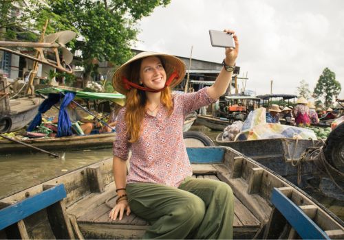 A tourist taking a selfie on a wooden boat at the Cai Rang Floating Market in Can Tho, Vietnam.