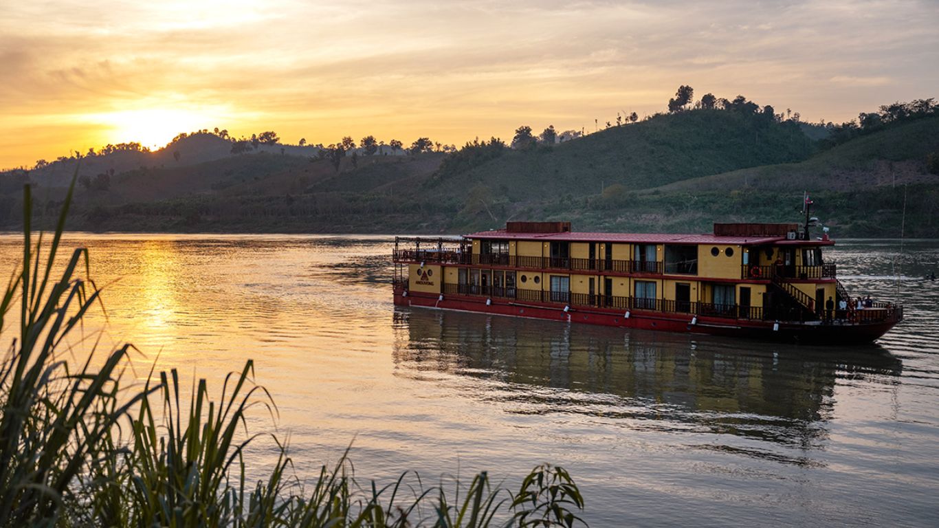 Private river cruise vessel sailing the Mekong at golden sunset in June.