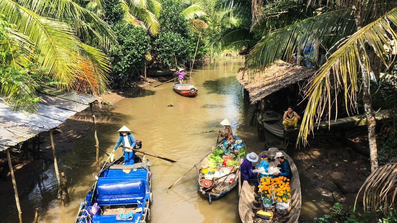 Local boats and vendors navigating a narrow canal lined with coconut palms in the Mekong Delta in June.
