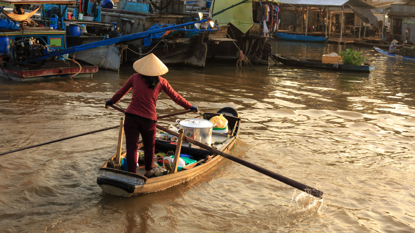 Woman in a conical hat rowing a sampan at Cai Rang floating market, a highlight of the Mekong Delta in November