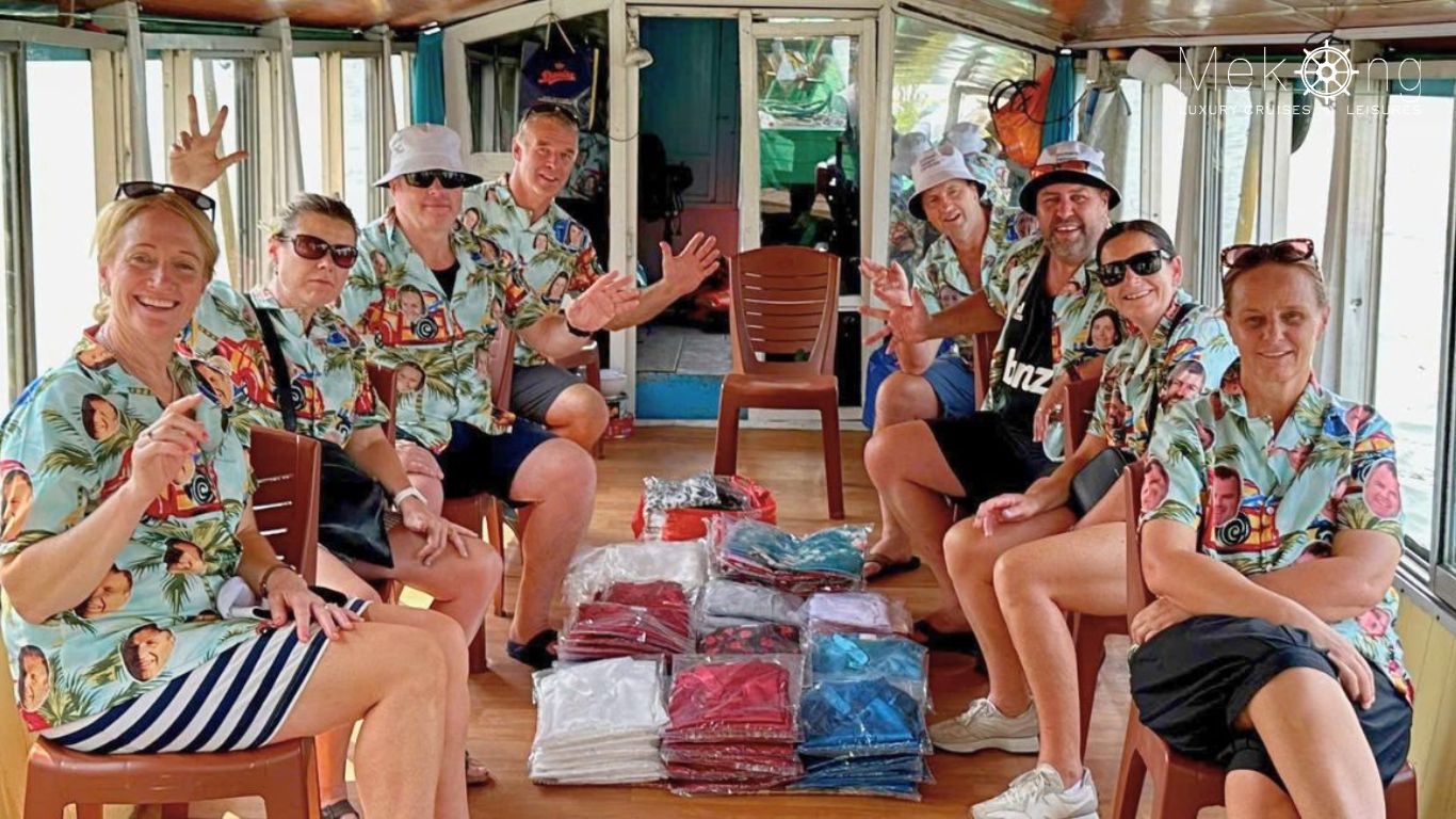 Smiling travelers in matching shirts sit together on a covered tour boat in the Mekong Delta